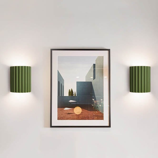 Framed artwork on a wall with two green sconces on either side.
