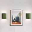 Framed artwork on a wall with two green sconces on either side.