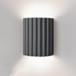 Black wall-mounted lamp with ribbed design on a gray wall