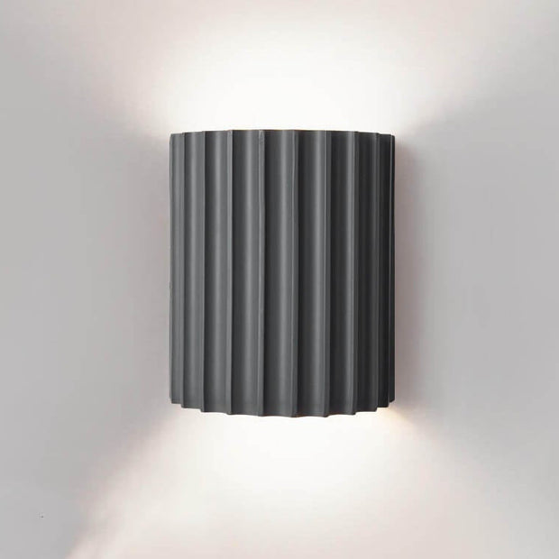 Black wall-mounted lamp with ribbed design on a gray wall