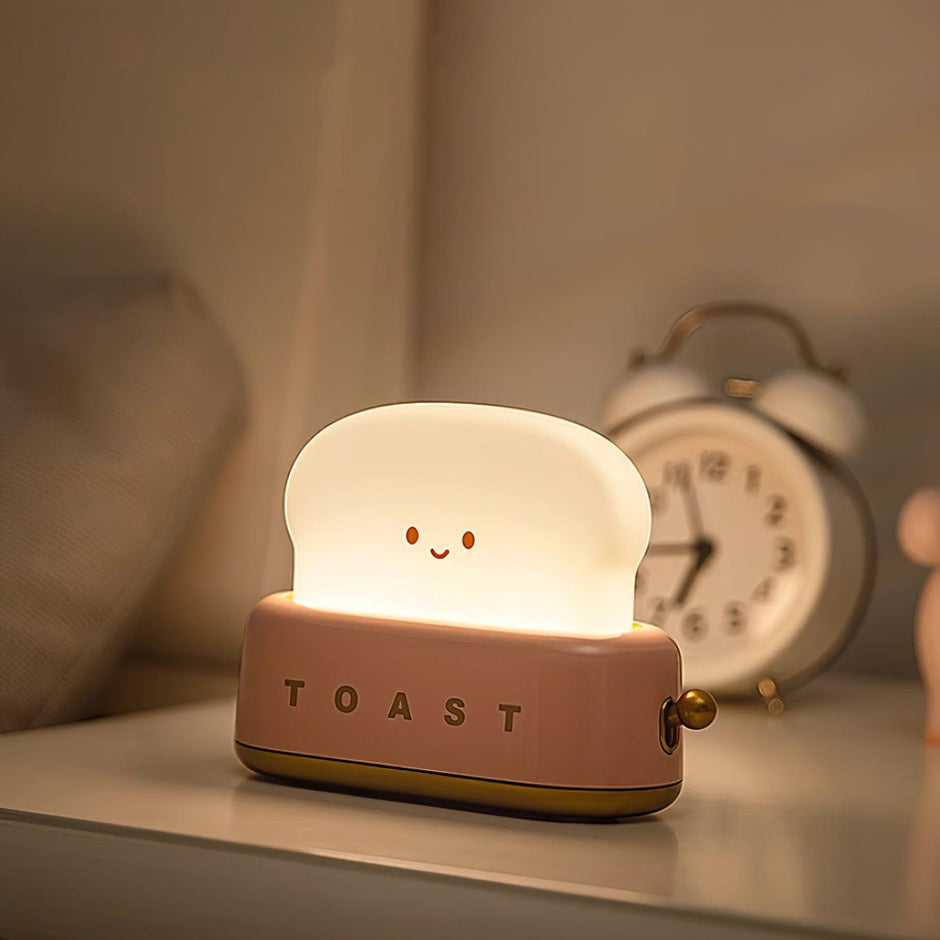 Pink night light shaped like a toaster with a smiling face on a shelf.