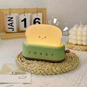 Toy toaster with a smiling face on a woven mat, with a calendar and decorative items in the background.
