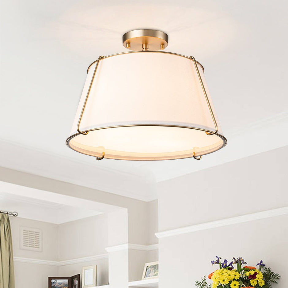 Ceiling light fixture with gold frame and white shade in a room setting.